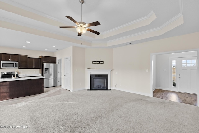 unfurnished living room featuring sink, crown molding, ceiling fan, light carpet, and a raised ceiling