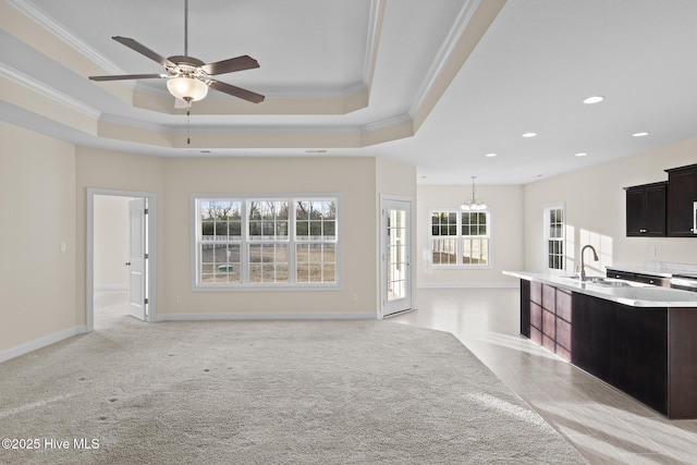 unfurnished living room featuring a raised ceiling, ornamental molding, sink, and ceiling fan with notable chandelier