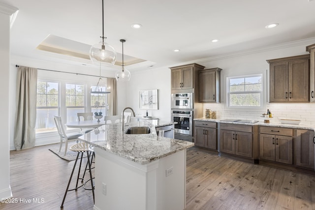 kitchen featuring a breakfast bar area, a sink, crown molding, backsplash, and a center island with sink