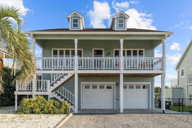 coastal home featuring covered porch, driveway, stairway, and an attached garage