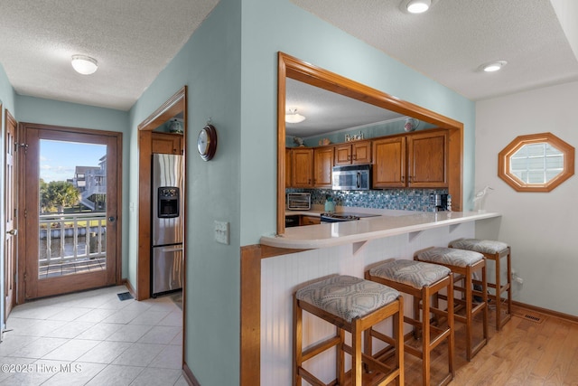 kitchen featuring a breakfast bar area, tasteful backsplash, light countertops, appliances with stainless steel finishes, and brown cabinetry