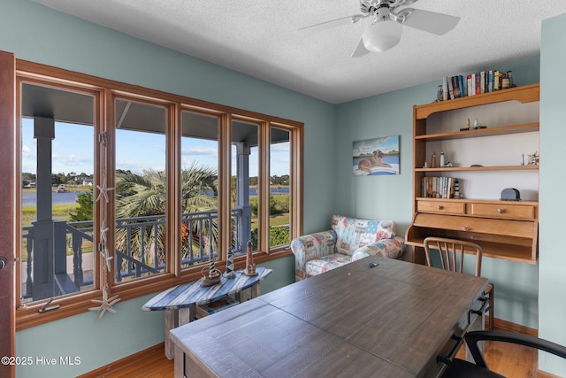 dining space featuring a ceiling fan, a textured ceiling, baseboards, and wood finished floors