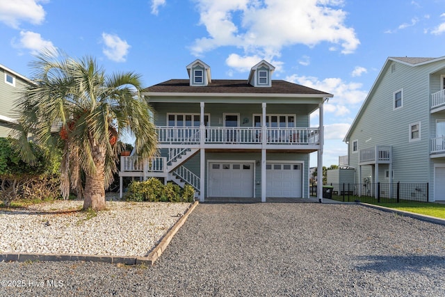 raised beach house with gravel driveway, an attached garage, stairs, and a porch