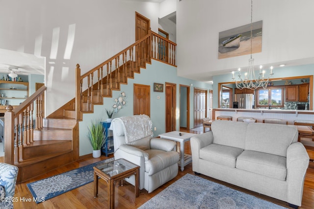 living area with stairs, a high ceiling, ceiling fan with notable chandelier, and wood finished floors