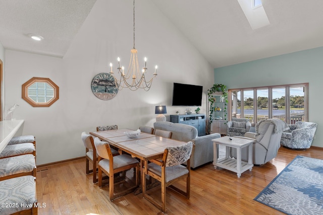 dining space featuring light wood finished floors, a skylight, baseboards, an inviting chandelier, and high vaulted ceiling