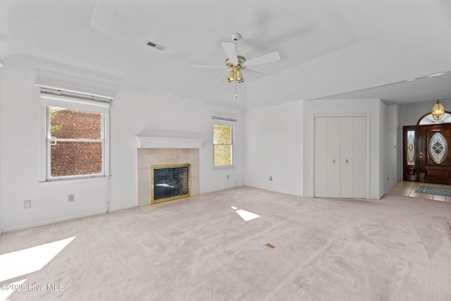 unfurnished living room featuring ceiling fan, light colored carpet, a tiled fireplace, and a textured ceiling