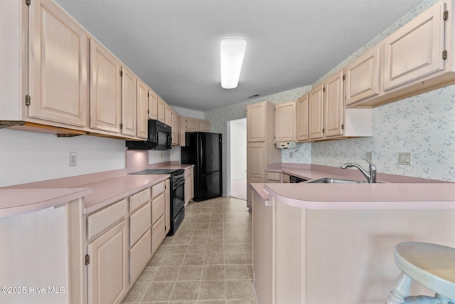 kitchen featuring sink, a breakfast bar area, black appliances, a textured ceiling, and kitchen peninsula