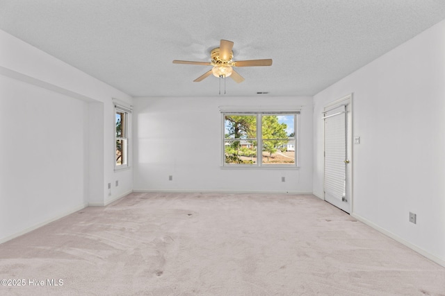 empty room with ceiling fan, light colored carpet, plenty of natural light, and a textured ceiling