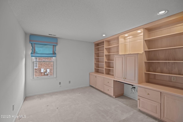 unfurnished office featuring built in desk, light carpet, and a textured ceiling