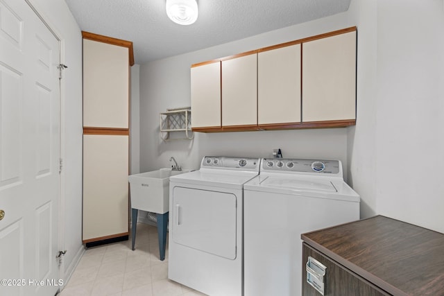 laundry area featuring cabinets, light tile patterned floors, a textured ceiling, and washing machine and clothes dryer