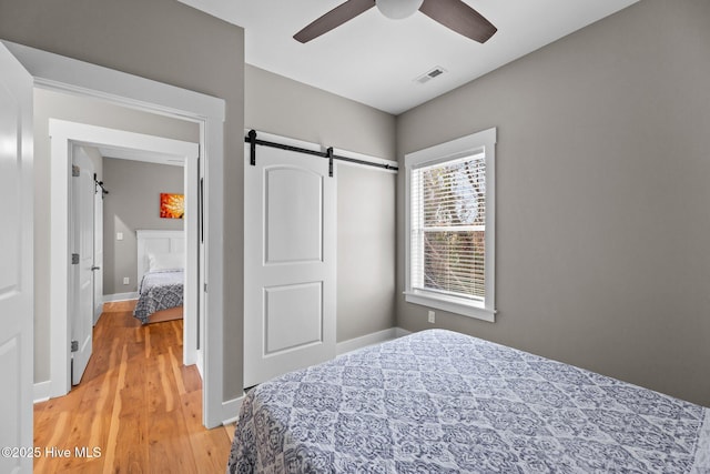 bedroom featuring wood-type flooring, a barn door, and ceiling fan