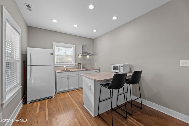 kitchen featuring wall chimney exhaust hood, a kitchen bar, sink, white cabinetry, and white appliances