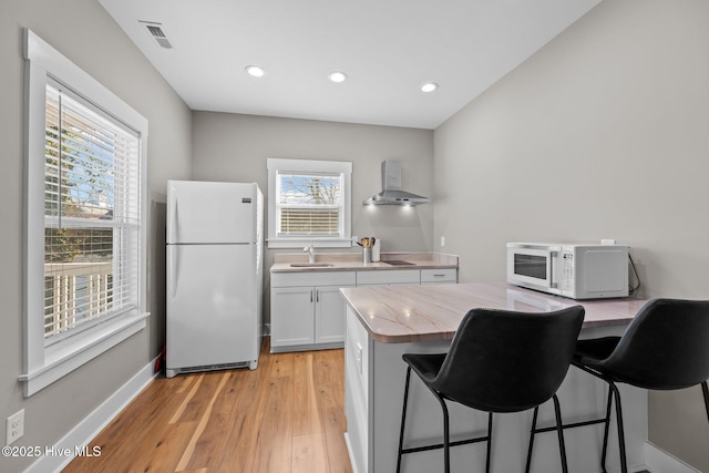 kitchen featuring sink, white cabinets, a kitchen breakfast bar, white appliances, and wall chimney exhaust hood