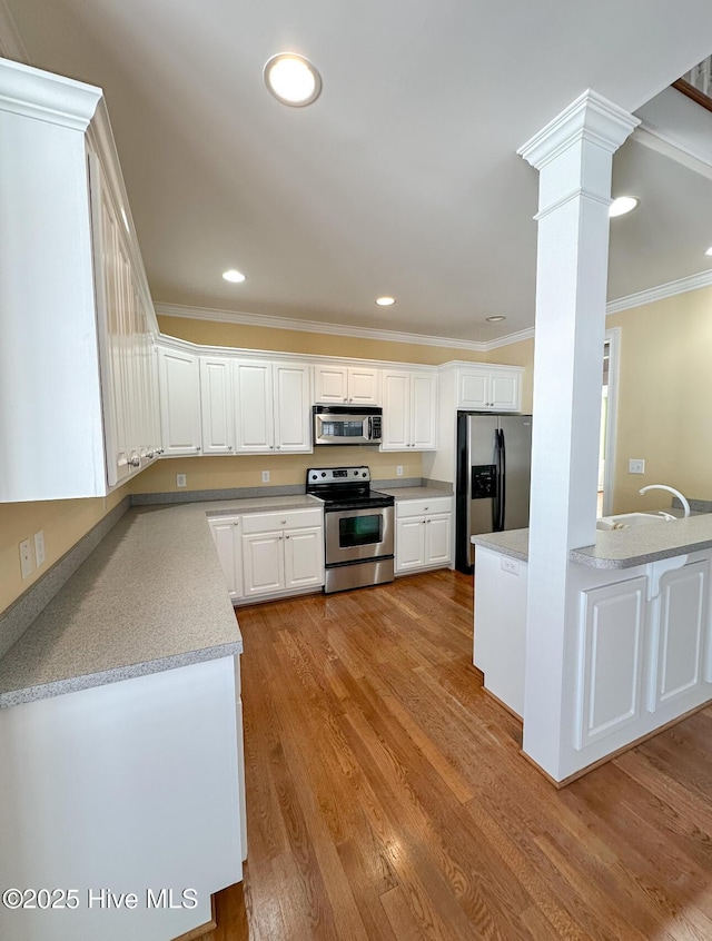 kitchen featuring white cabinetry, stainless steel appliances, ornate columns, ornamental molding, and light wood-type flooring