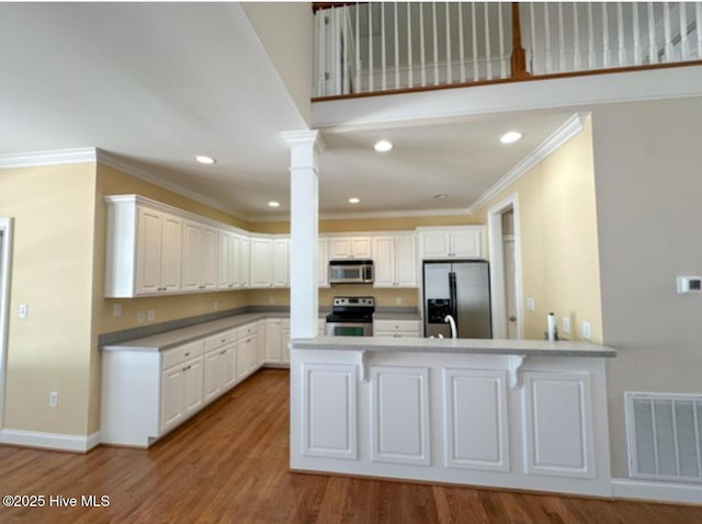 kitchen with appliances with stainless steel finishes, hardwood / wood-style floors, white cabinets, kitchen peninsula, and ornate columns