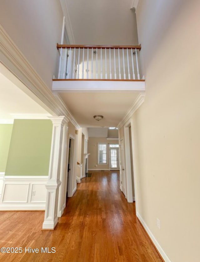 corridor with ornamental molding, decorative columns, wood-type flooring, and a high ceiling