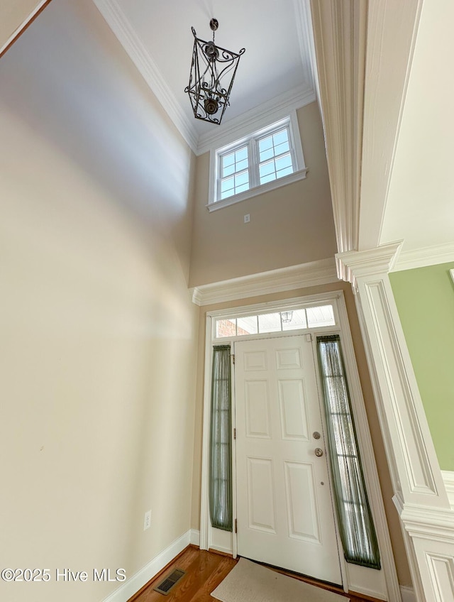 foyer with crown molding, hardwood / wood-style floors, a high ceiling, and a notable chandelier