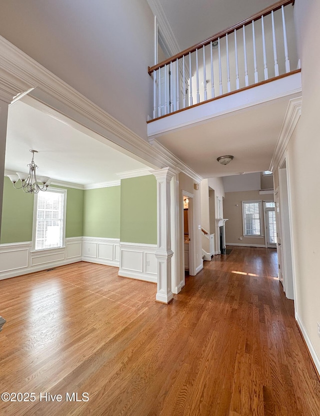 unfurnished living room with crown molding, a healthy amount of sunlight, hardwood / wood-style floors, and decorative columns