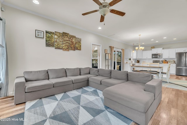 living room featuring ornamental molding, ceiling fan with notable chandelier, and light wood-type flooring