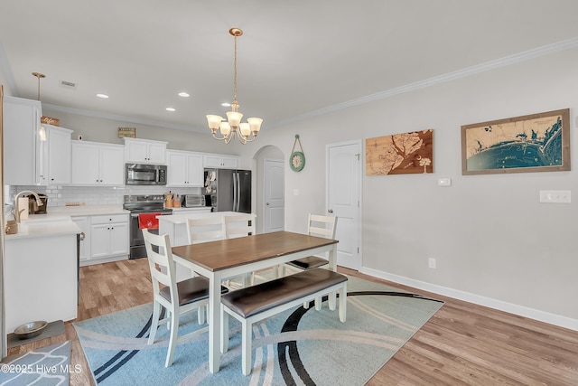 dining area featuring ornamental molding, light hardwood / wood-style floors, sink, and a notable chandelier