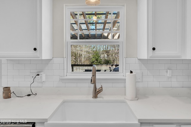 interior details with tasteful backsplash, sink, light stone countertops, and white cabinets