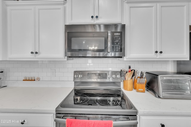 kitchen with stainless steel appliances, light stone countertops, white cabinets, and backsplash