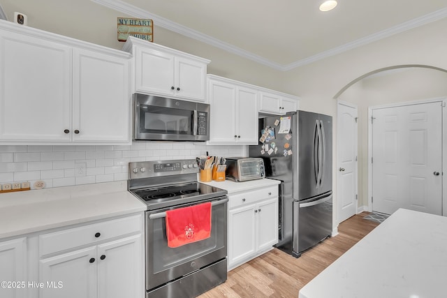 kitchen with white cabinets, backsplash, stainless steel appliances, crown molding, and light hardwood / wood-style flooring