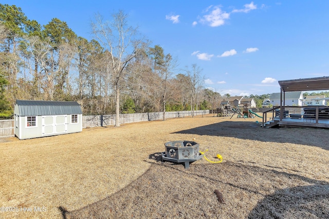 view of yard with a wooden deck, a storage unit, a playground, and an outdoor fire pit