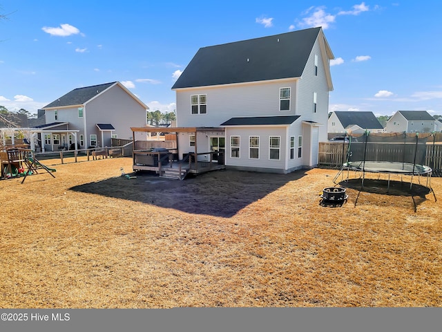 back of house with a wooden deck, a playground, and a trampoline