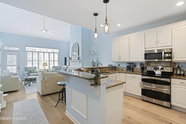 kitchen featuring sink, a breakfast bar area, appliances with stainless steel finishes, white cabinetry, and decorative light fixtures