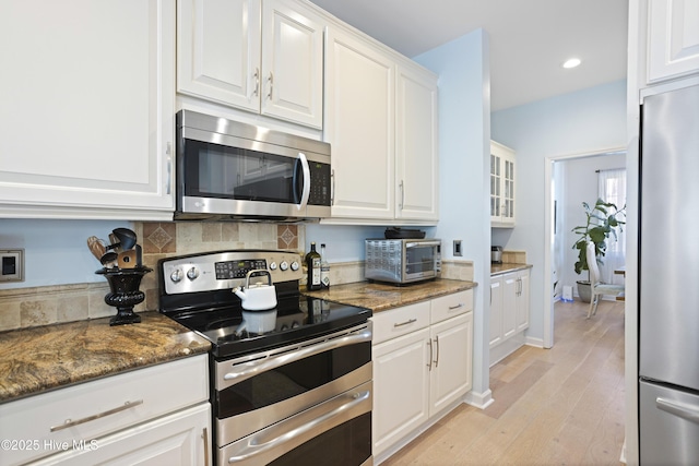 kitchen featuring tasteful backsplash, white cabinetry, dark stone counters, stainless steel appliances, and light hardwood / wood-style flooring