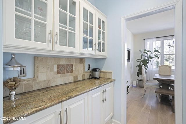 bar featuring tasteful backsplash, white cabinetry, dark stone countertops, and light wood-type flooring