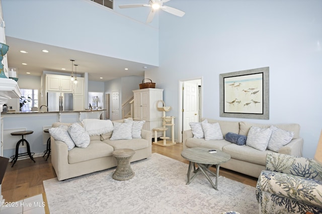 living room with a high ceiling, ceiling fan, and light hardwood / wood-style flooring