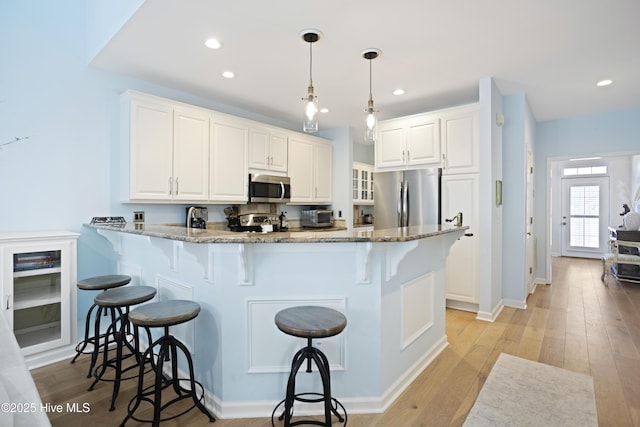 kitchen featuring white cabinetry, hanging light fixtures, stainless steel appliances, light stone countertops, and kitchen peninsula