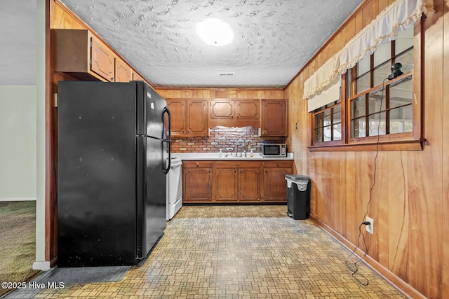 kitchen with sink, wood walls, black fridge, a textured ceiling, and stove