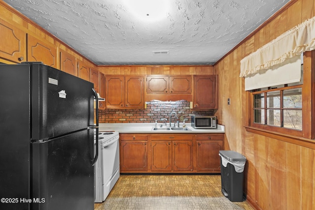 kitchen featuring sink, black refrigerator, white electric range oven, and wood walls