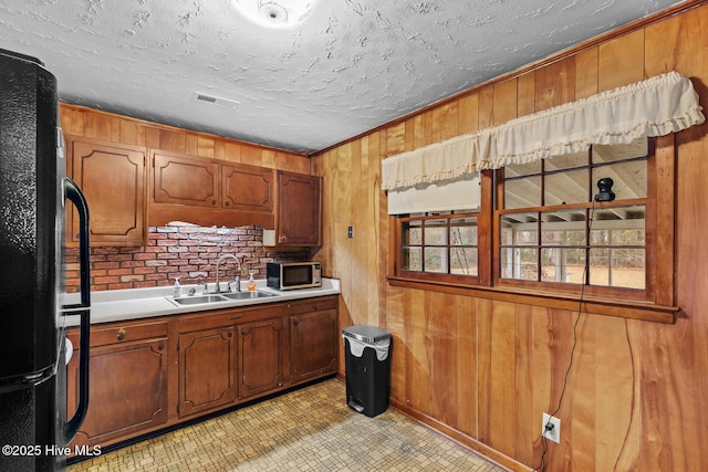 kitchen featuring black refrigerator, ornamental molding, sink, and wood walls