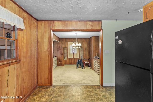 interior space with pendant lighting, black refrigerator, a textured ceiling, a chandelier, and wood walls