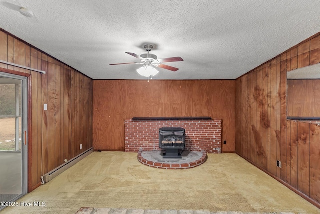 unfurnished living room with a baseboard heating unit, wooden walls, a textured ceiling, light carpet, and a wood stove