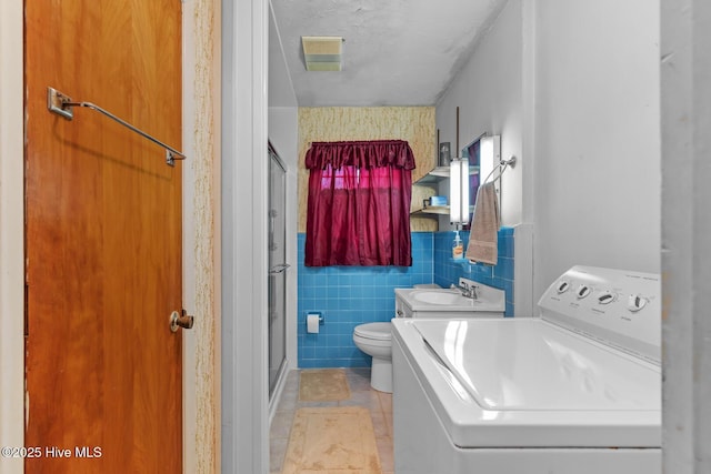 bathroom featuring tile patterned flooring, tile walls, vanity, an enclosed shower, and washer / dryer