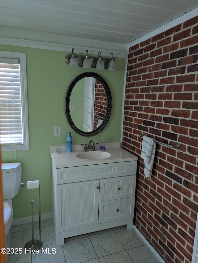 bathroom featuring vanity, crown molding, toilet, and brick wall