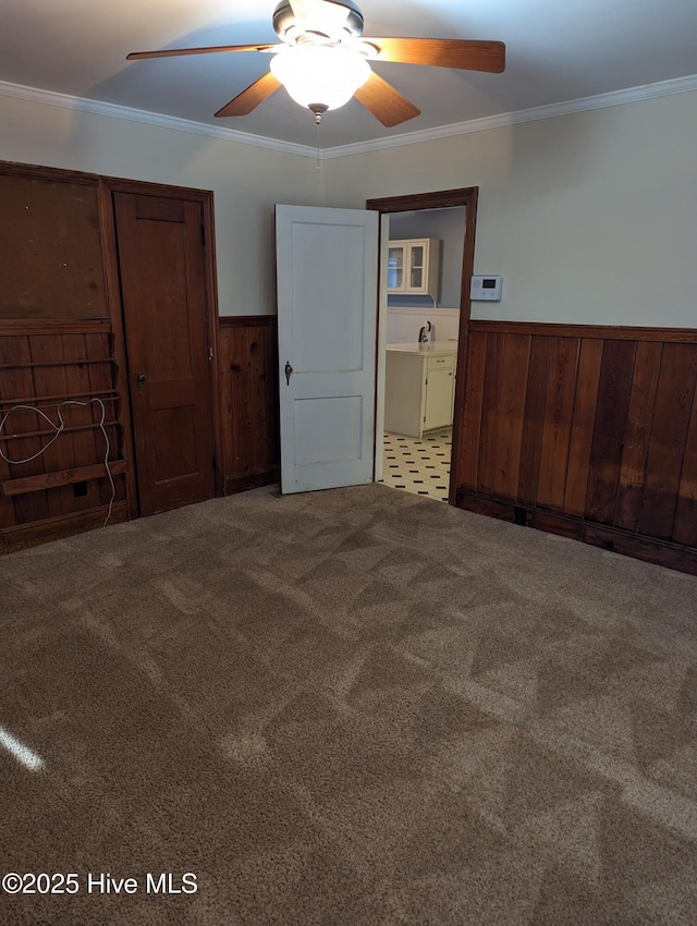 unfurnished bedroom featuring crown molding, carpet flooring, sink, and wood walls