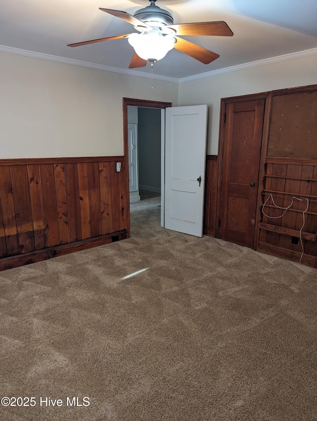 unfurnished bedroom featuring crown molding, wood walls, ceiling fan, and carpet