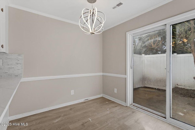 unfurnished dining area featuring hardwood / wood-style flooring, ornamental molding, and an inviting chandelier