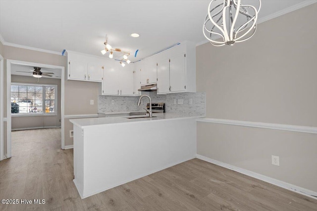 kitchen with sink, ornamental molding, kitchen peninsula, pendant lighting, and white cabinets