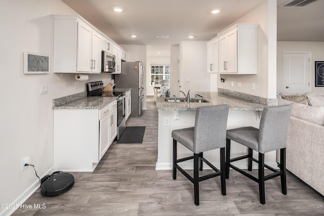 kitchen featuring appliances with stainless steel finishes, white cabinets, a kitchen bar, and kitchen peninsula