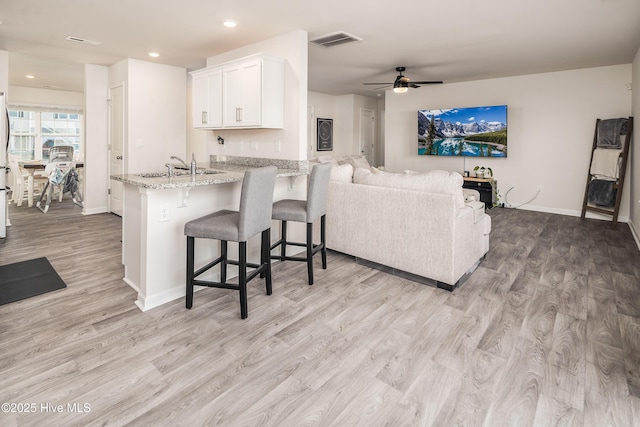 kitchen featuring a breakfast bar, white cabinetry, light hardwood / wood-style floors, kitchen peninsula, and light stone countertops