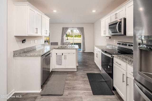 kitchen featuring hardwood / wood-style flooring, stainless steel appliances, light stone countertops, white cabinets, and kitchen peninsula