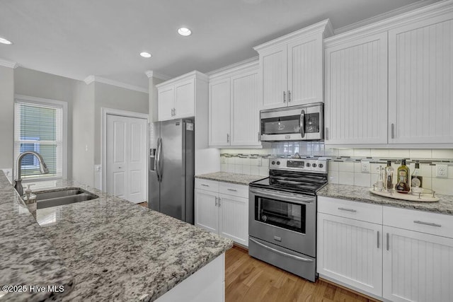 kitchen featuring light stone counters, appliances with stainless steel finishes, ornamental molding, white cabinetry, and a sink