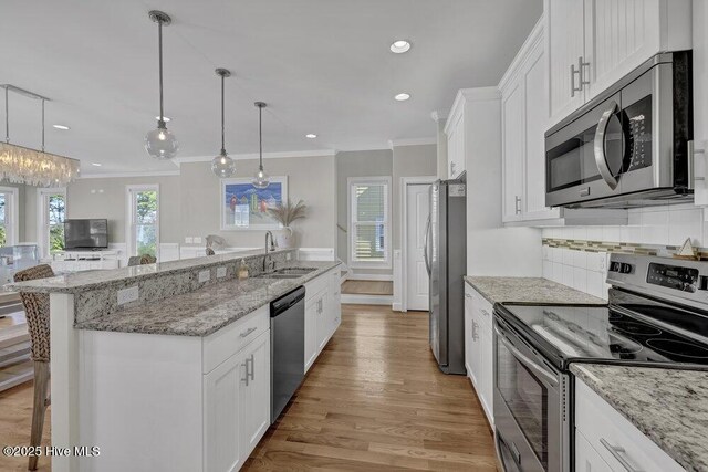 kitchen featuring decorative light fixtures, white cabinetry, an island with sink, sink, and stainless steel appliances